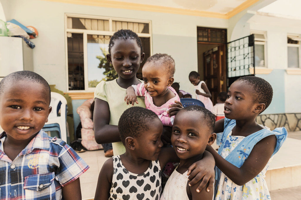 Children stand smiling in front of a house and look into the camera.