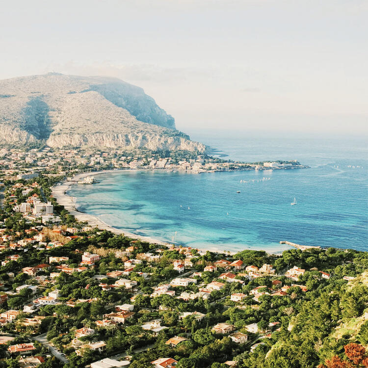 Eine atemberaubende Aufnahme des Strands von Mondello, bei der sich das helle Sandufer unter dem blauen Mittelmeer und den majestätischen Felsformationen erstreckt.