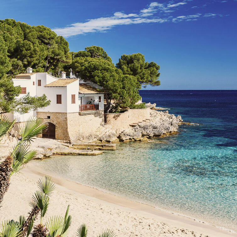 A bay in Majorca with white sandy beach and a finca on top of the cliffs