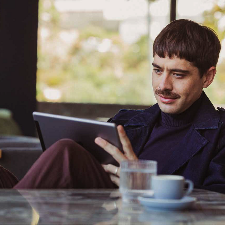 A man sits in a lounge with a laptop and coffee