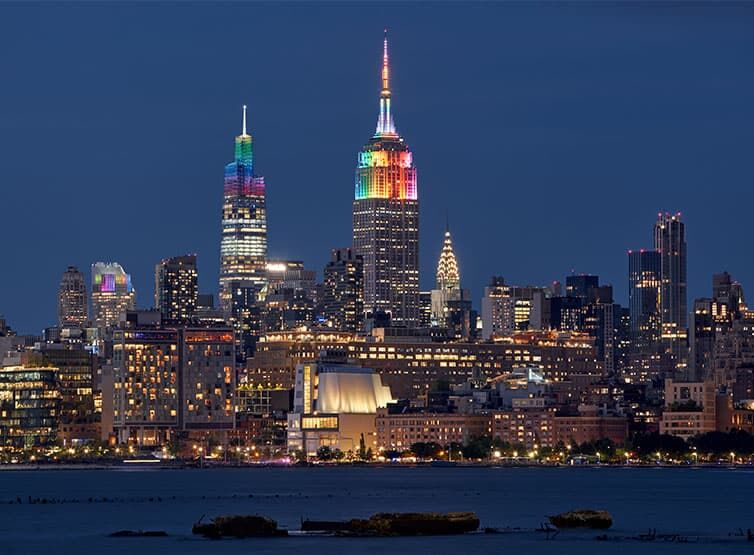 The famous New York skyline at night, some skyscrapers and landmarks glow in rainbow colors for NYC Pride
