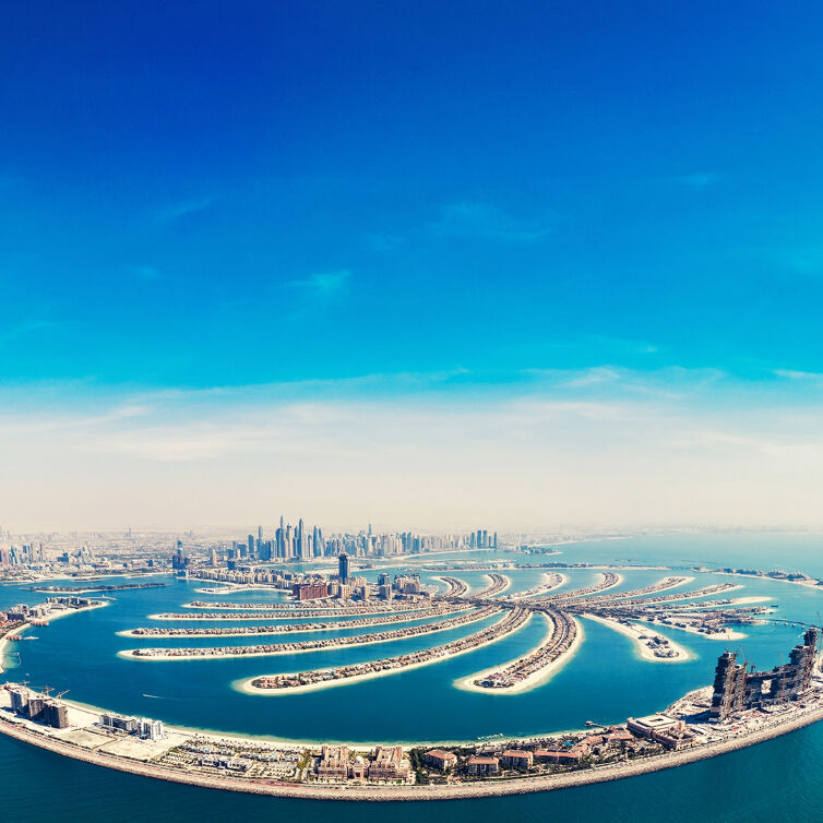 Aerial view of the Palm Jumeirah in Dubai, showcasing its unique palm tree-like structure with luxury homes lining the fronds, surrounded by the azure waters of the Persian Gulf