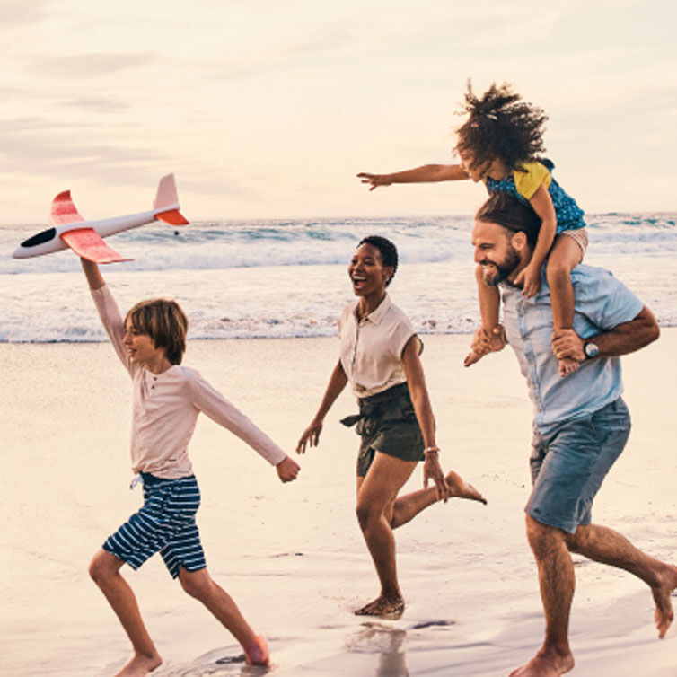 A family runs across a beach laughing, the boy holds a model aeroplane in his hand