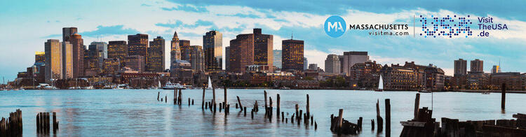 Panoramic view of the Boston skyline at dusk with buildings illuminated against the evening sky, 