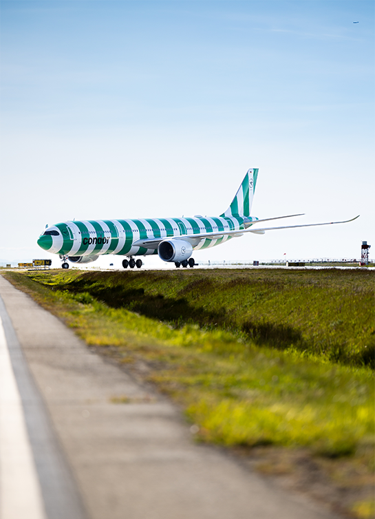 Side view of Condor’s green-striped A330neo aircraft preparing for takeoff on runway, with wing flex and tail fin visible.