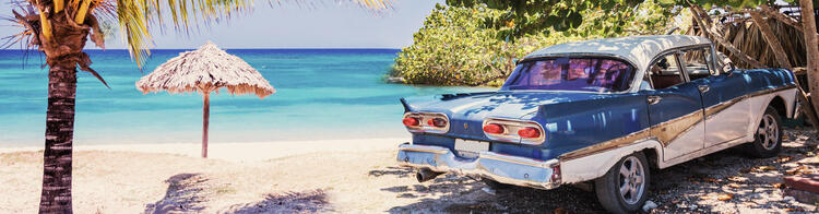 Vieille voiture bleue sur la plage avec palem et parapluie de paille