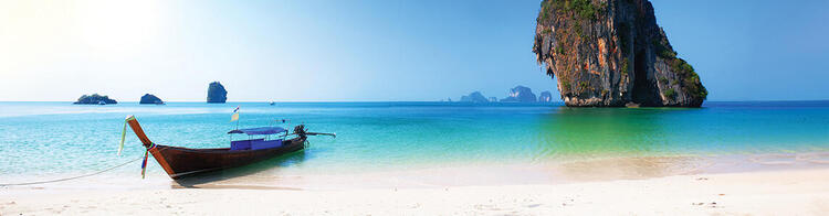 Un paysage tranquille avec un bateau longtail ancré sur le sable blanc d'une plage en Thaïlande, avec des eaux cristallines turquoise.