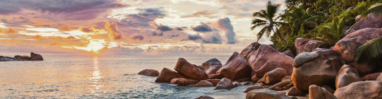 Tramonto mozzafiato su una spiaggia delle Seychelles con rocce granitiche, sabbia bianca e palme tropicali