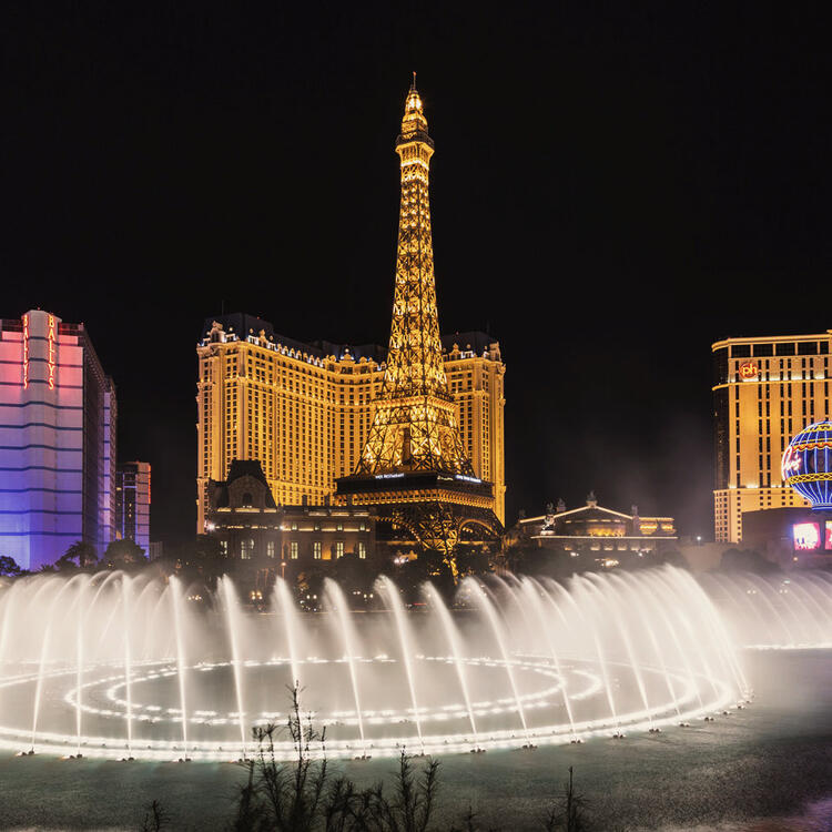 Spettacolo notturno delle fontane del Bellagio a Las Vegas, con la replica illuminata della Torre Eiffel del Paris Las Vegas sullo sfondo.