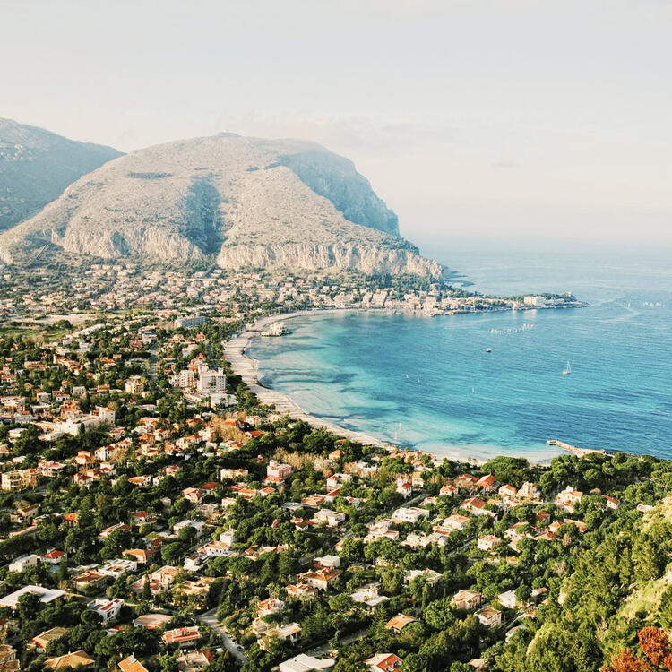 Monte Pellegrino Palermo, Italia Vista panoramica su Mondello, Palermo: mare cristallino, spiaggia dorata e montagne sullo sfondo.