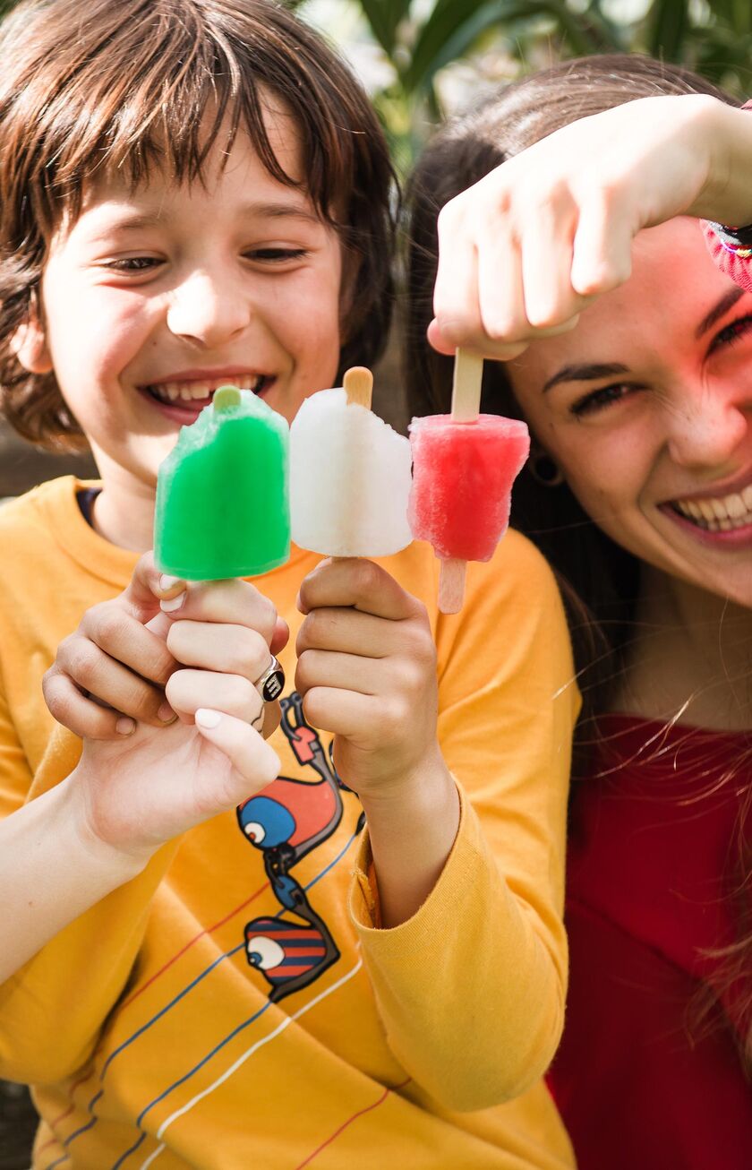 Un bambino e due donne sorridono mentre gustano ghiaccioli verde, bianco e rosso durante una calda giornata estiva
