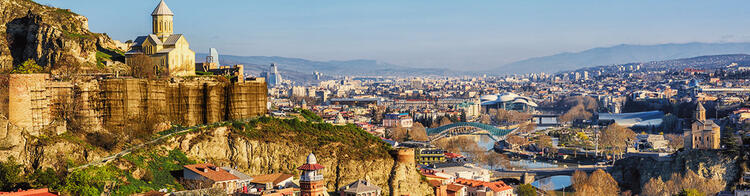 Veduta panoramica di Tbilisi, Georgia, con la Fortezza di Narikala, il Ponte della Pace e le colline sullo sfondo.