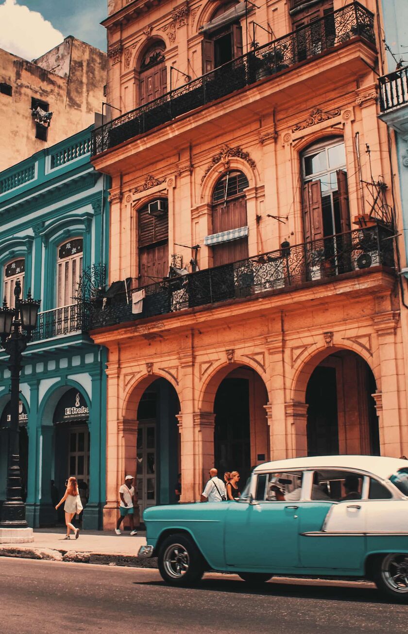 Un'auto d'epoca color turchese si trova davanti a una fila di case colorate a L'Avana, Cuba.