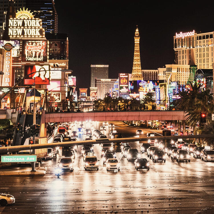 Vista notturna della Las Vegas Strip con traffico intenso, insegne luminose, il casinò New York-New York e la replica della Torre Eiffel del Paris Las Vegas sullo sfondo.