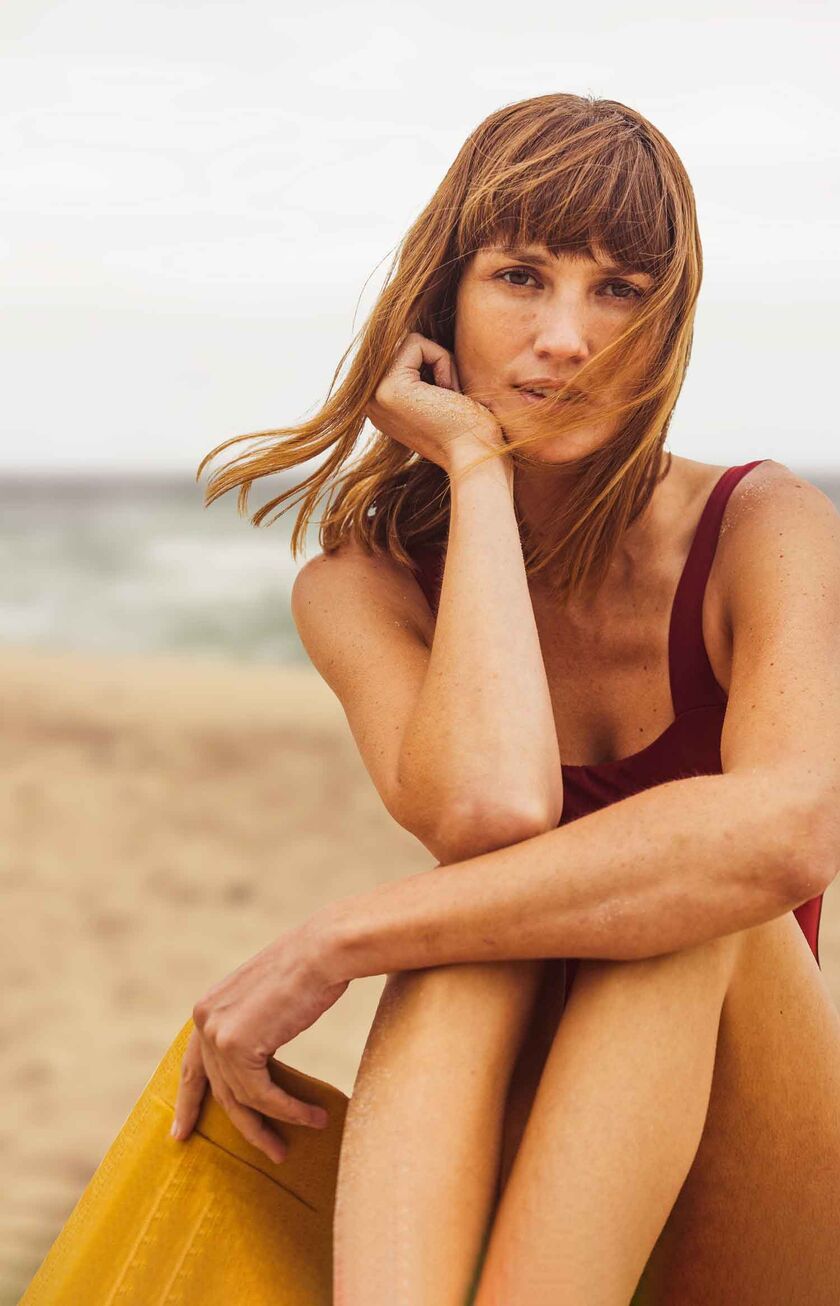 Una donna seduta in costume da bagno sulla spiaggia guarda sognante nella telecamera