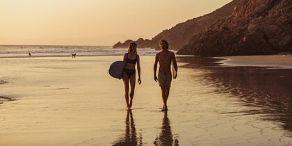 Twee surfers lopen langs het strand bij zonsondergang