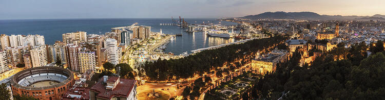 Een panoramisch uitzicht op Malaga tijdens zonsondergang, met de stierenvechtersarena op de voorgrond, omringd door lichtgevende stadslichten