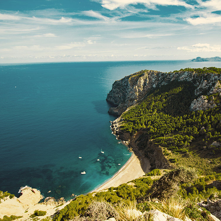 Prachtig uitzicht op de kust in Mallorca met een steile, weelderige klif met uitzicht op de diepblauwe zee onder een gedeeltelijk bewolkte lucht, wat duidt op een rustige en schilderachtige natuurlijke omgeving.