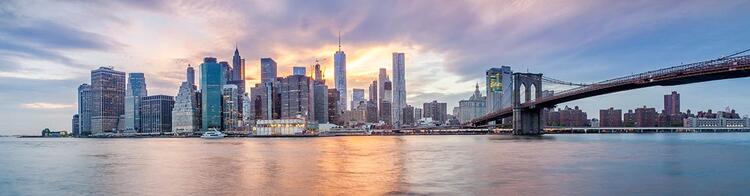 Panorama do horizonte de Nova Iorque ao crepúsculo com a Ponte do Brooklyn à direita e reflexos das luzes da cidade na água