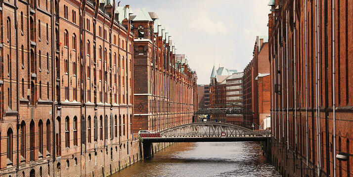 Speicherstadt em Hamburgo | Condor anal estreito da Speicherstadt em Hamburgo, ladeado por armazéns históricos de tijolos com ponte de metal, refletindo a herança marítima e a arquitetura industrial da cidade