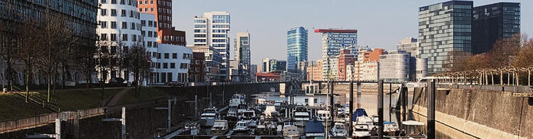 Vista panorâmica do Media Harbour em Düsseldorf, Alemanha, com edifícios modernos de arquitetura inovadora ao longo do cais e barcos ancorados em um dia claro