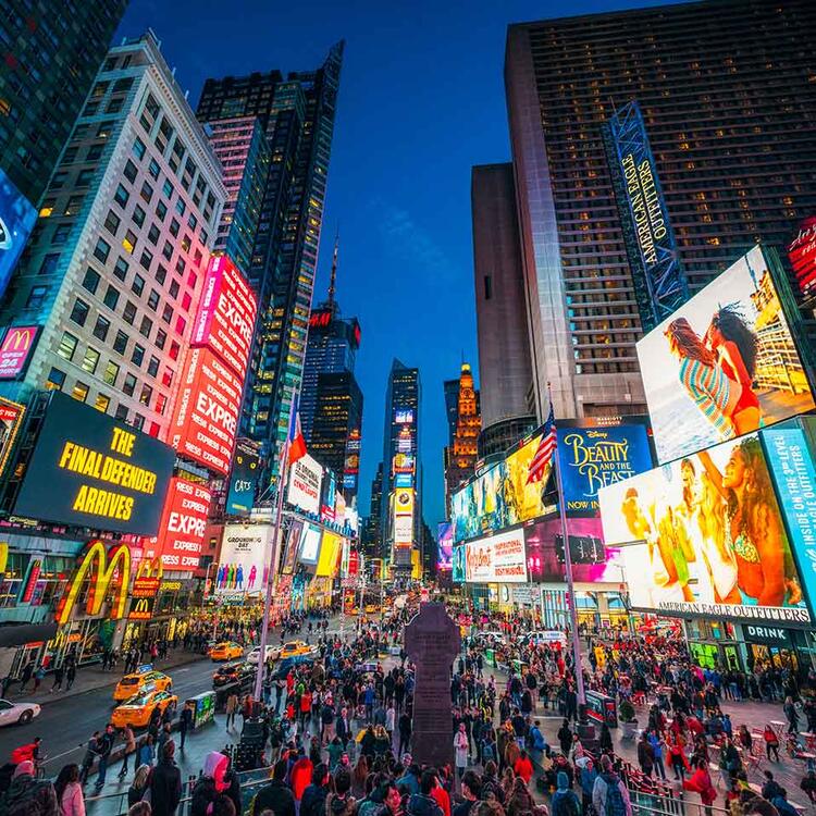 Times Square à noite, repleto de luzes neon, anúncios luminosos, táxis amarelos e multidões de pessoas caminhando na área pedestre.