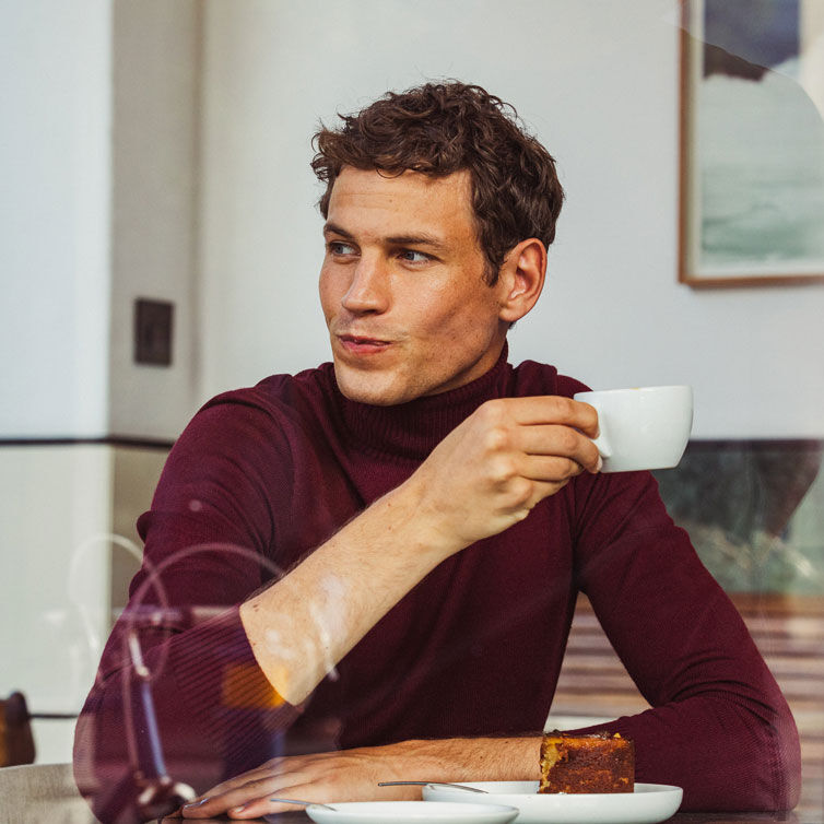 Um homem senta-se com uma chávena de café na mesa de pequeno-almoço de um hotel.