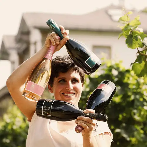 Winzerin hält Weinflaschen hoch, in denen sich die Sonne bricht