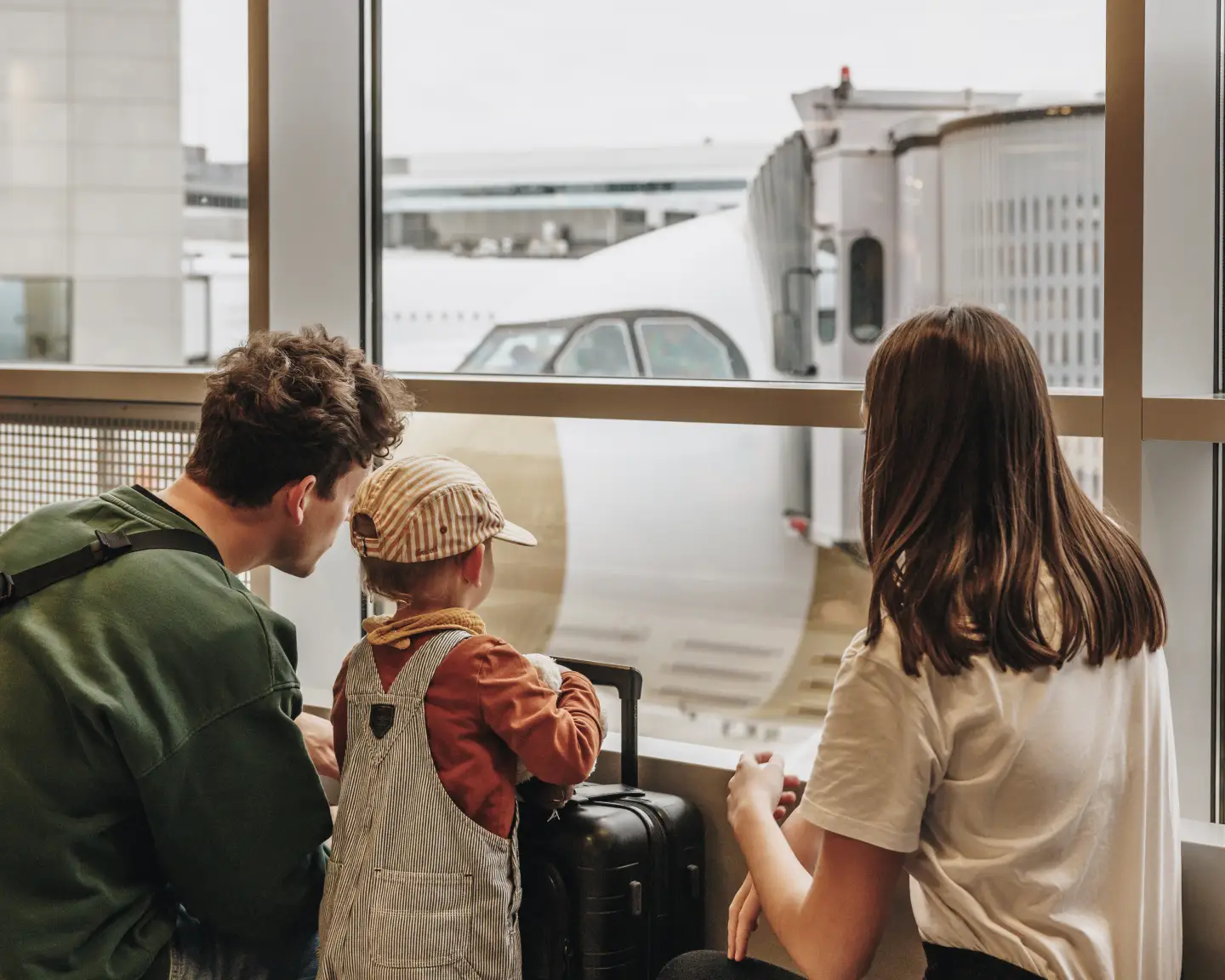 Un père, une mère et un enfant en bas âge regardent la piste depuis le bâtiment de l'aéroport