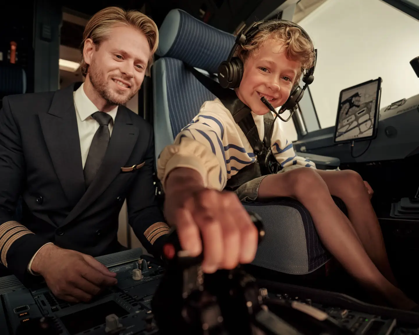 Un piloto y un niño sentados juntos en la cabina de un avión y accionando la palanca de despegue.