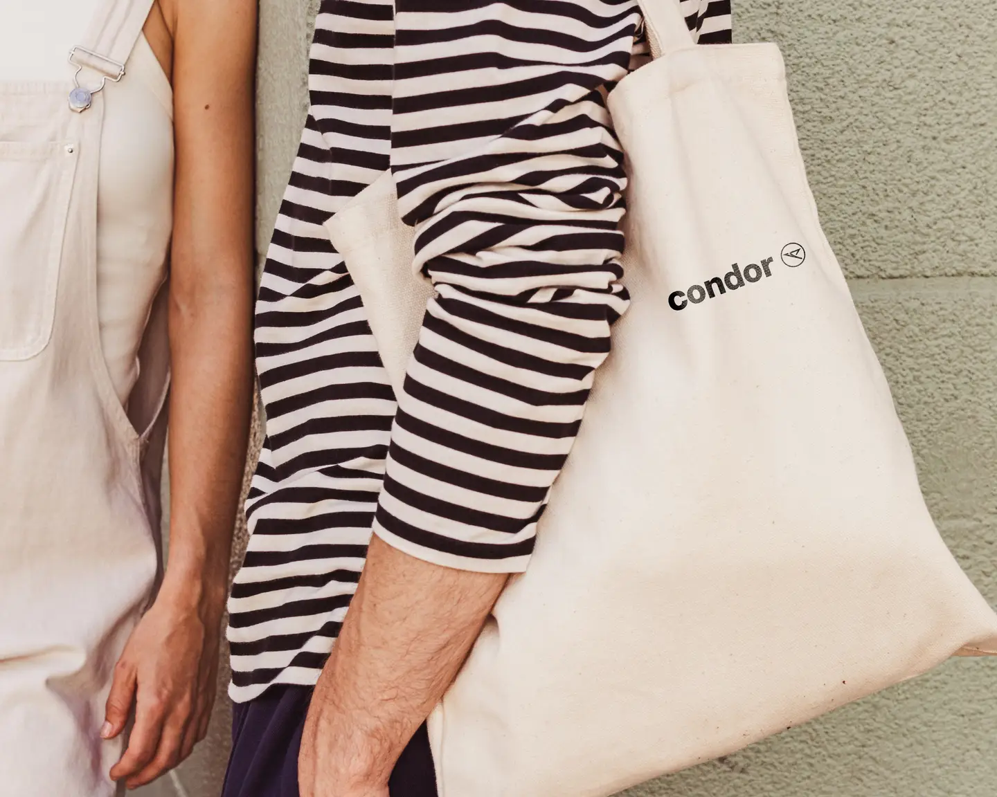 Detalle de una bolsa de lona con el logotipo de Condor colgada del hombro de una persona.