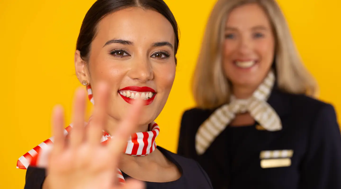 Dos auxiliares de vuelo sonrientes delante de un fondo amarillo