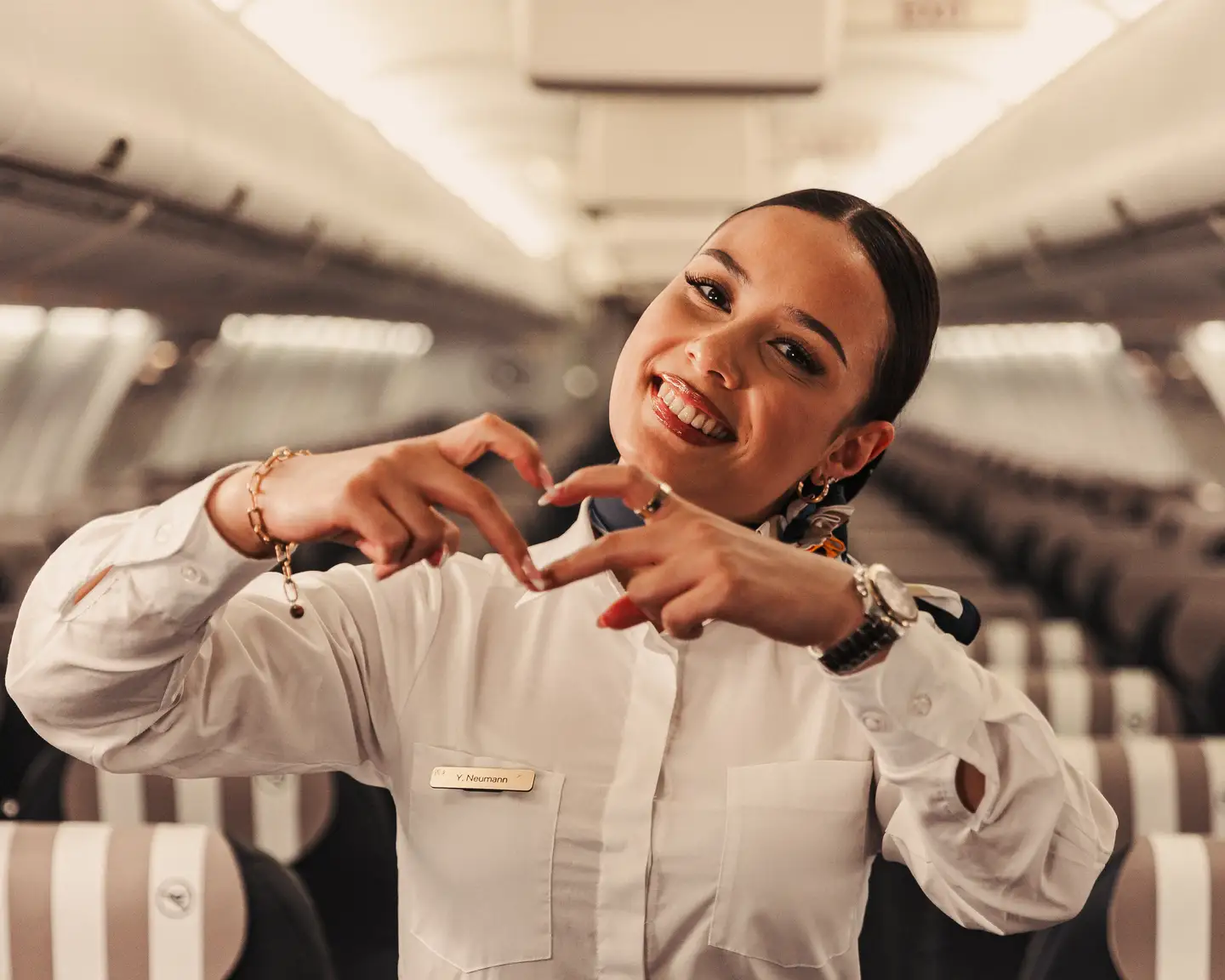 Auxiliar de vuelo sonriente de pie en un avión, formando un corazón con los dedos.