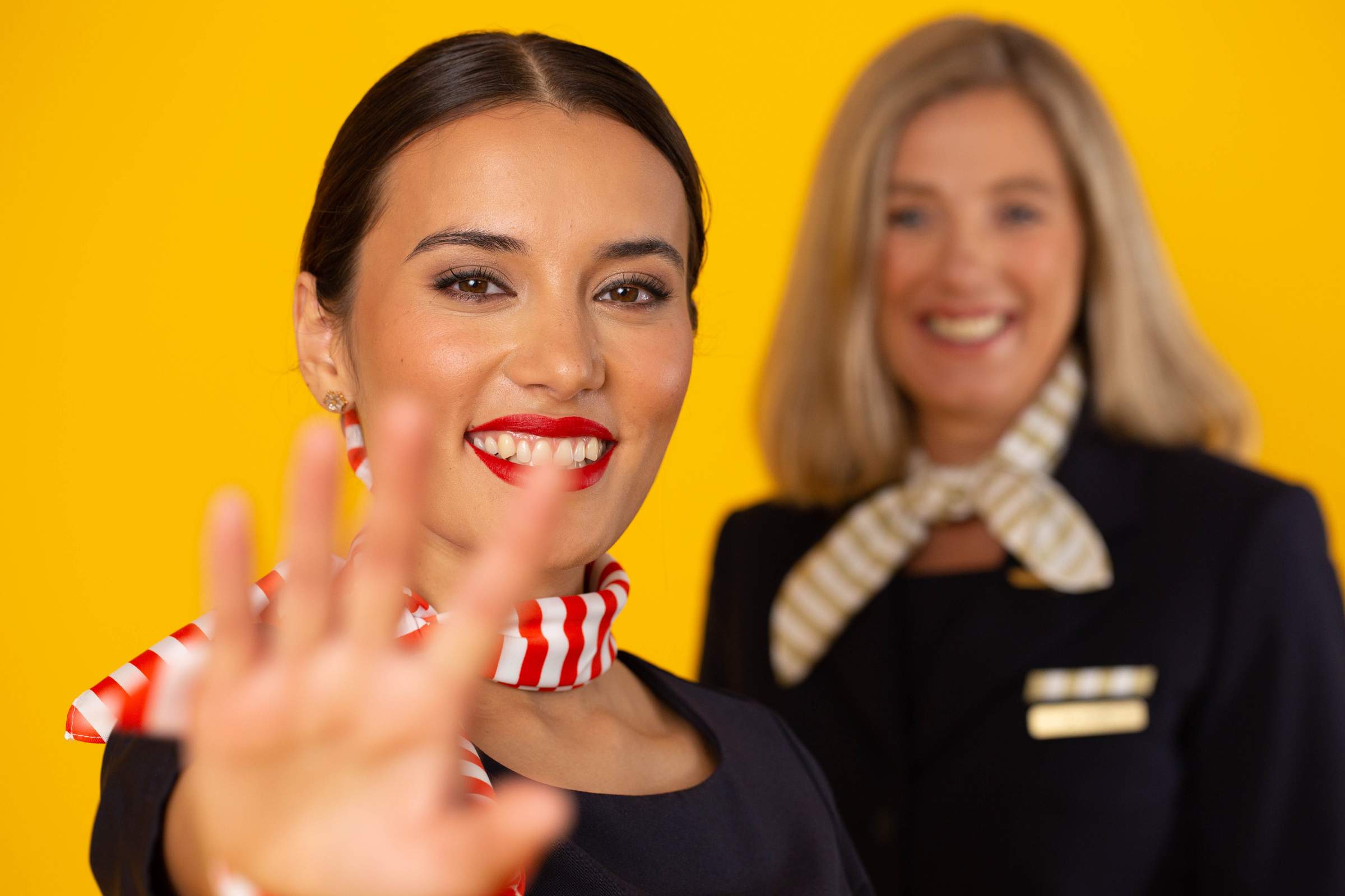 Dos auxiliares de vuelo sonrientes delante de un fondo amarillo