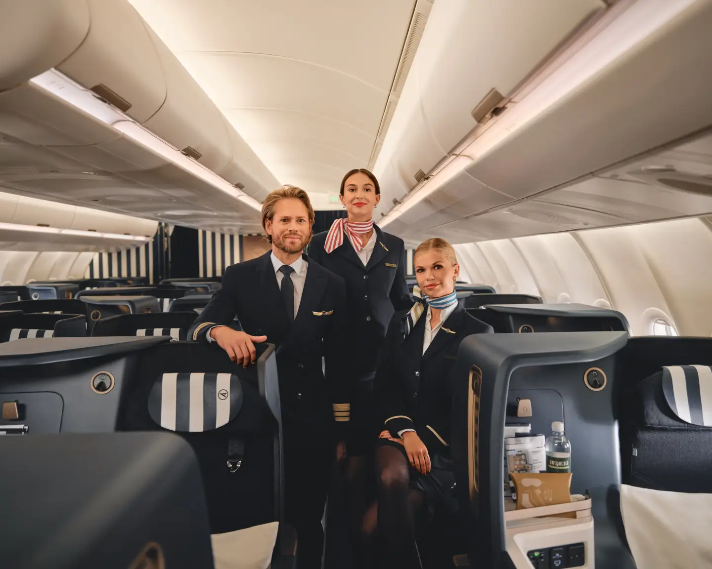 Dos auxiliares de vuelo y un piloto, todos con uniforme de Condor, de pie en el pasillo de la Business Class del Airbus A330neo