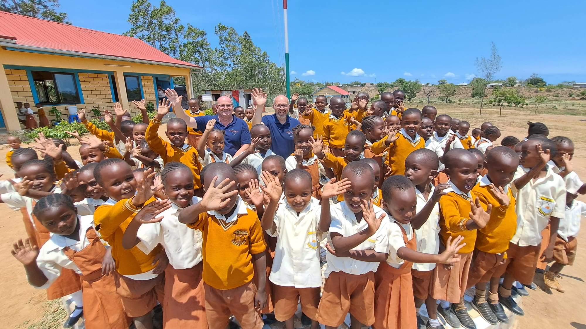 Skupina dětí v Africe s členy organizace Wir helfen in Afrika (We Help in Africa) e.V. v pozadí