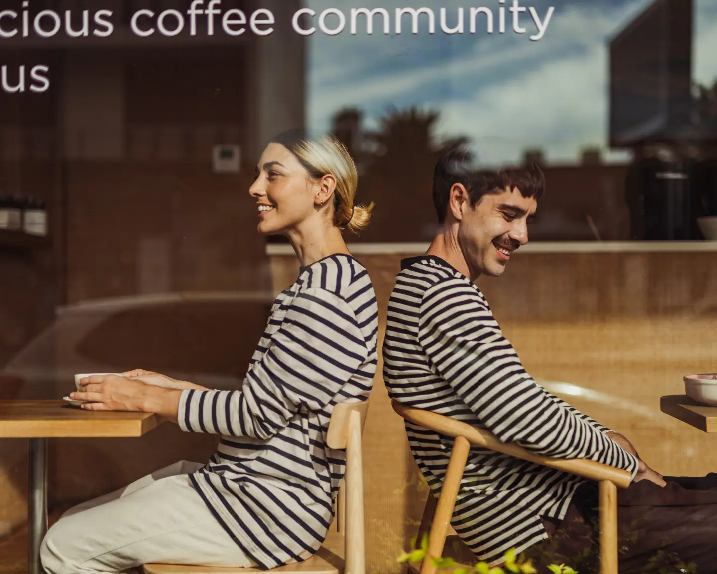 Deux jeunes gens sont assis dos à dos dans un café, vêtus de t-shirts rayés.