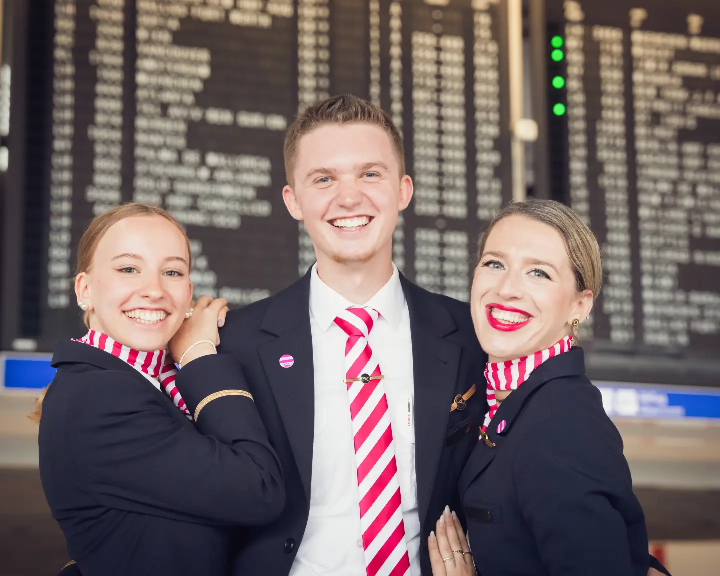 Condor Crew in dunkelblauer Uniform mit pink gestreiften FlyPink Accessoires posiert am Flughafen.