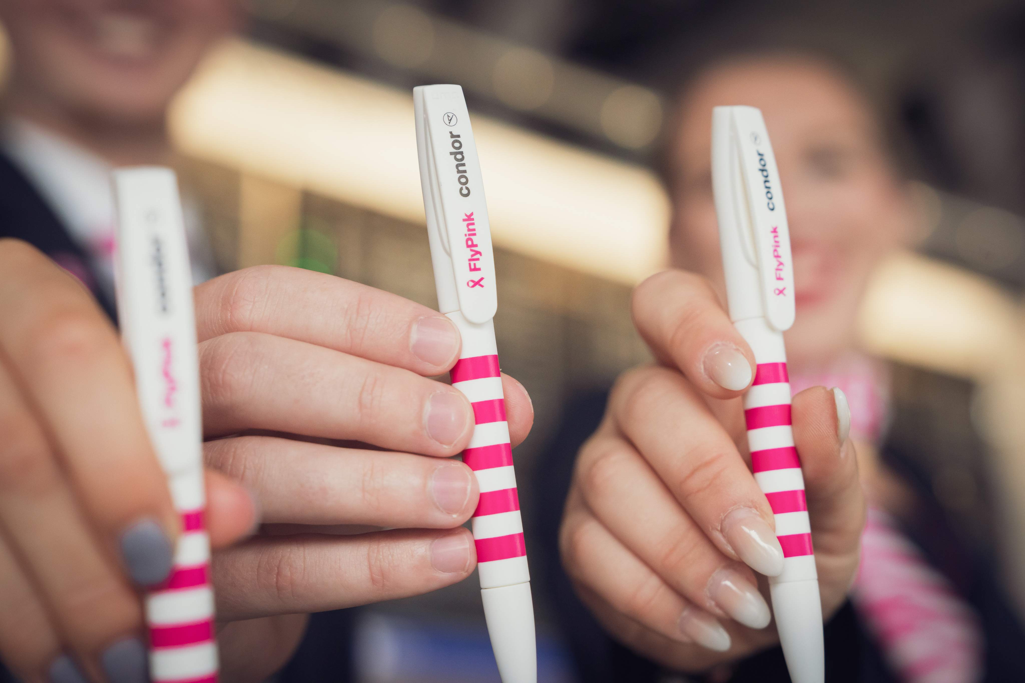 Close-up of two hands showing white-pink striped Condor pens with “Flypink” print