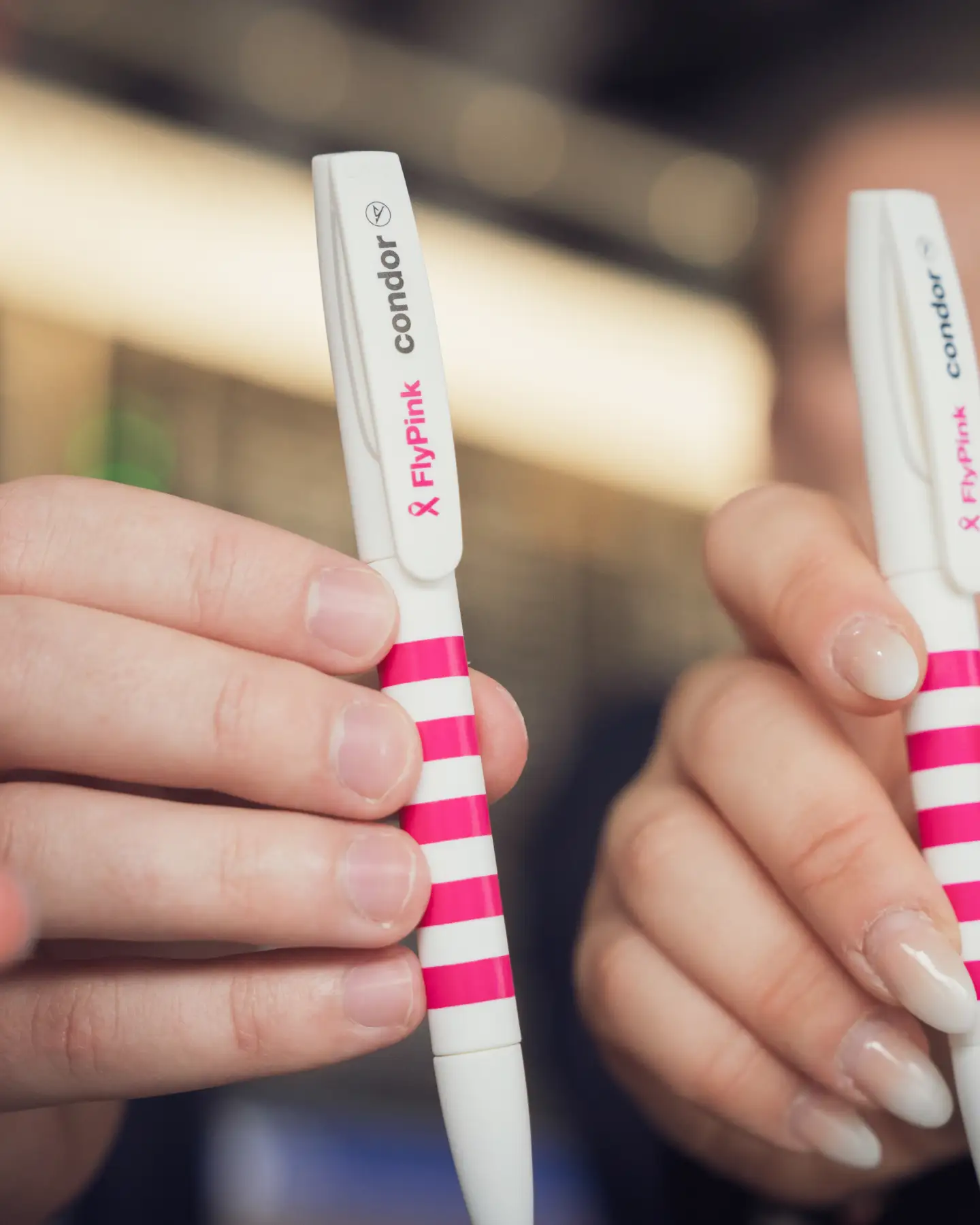 Close-up of two hands showing white-pink striped Condor pens with “Flypink” print