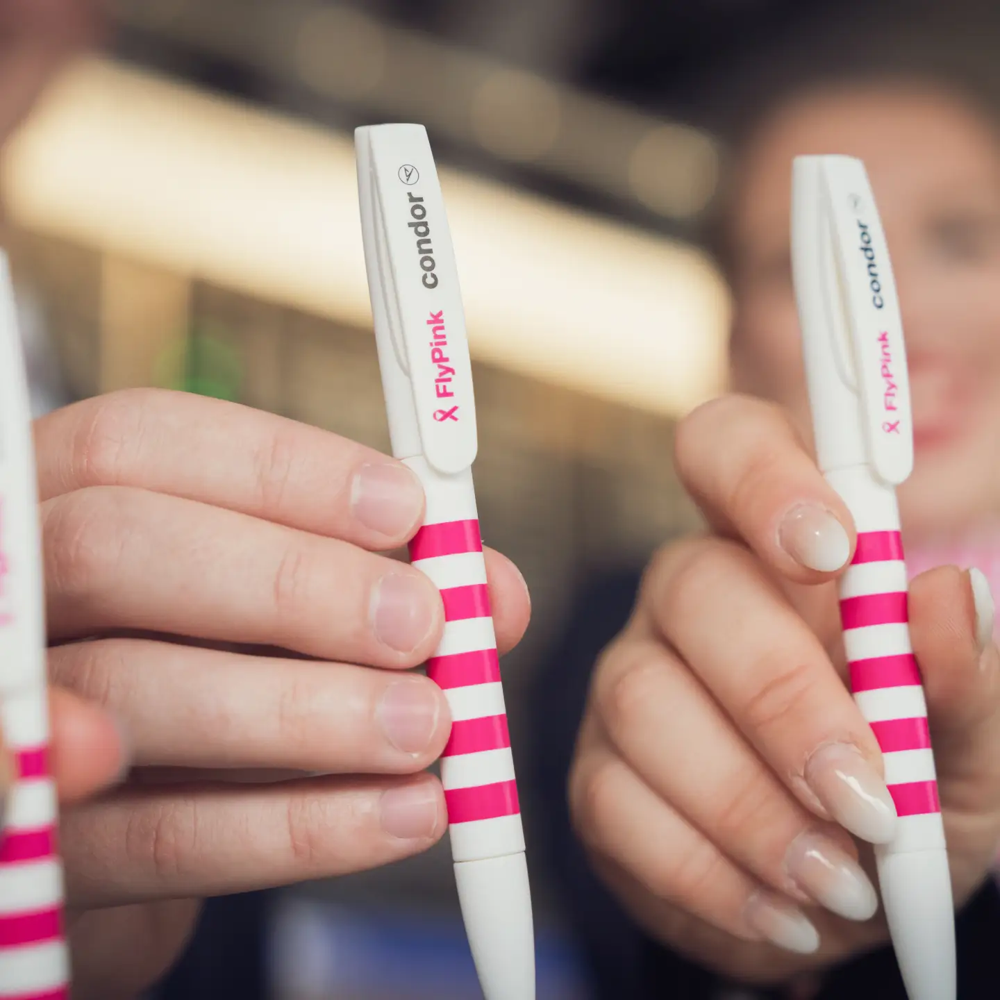 Close-up of two hands showing white-pink striped Condor pens with “Flypink” print