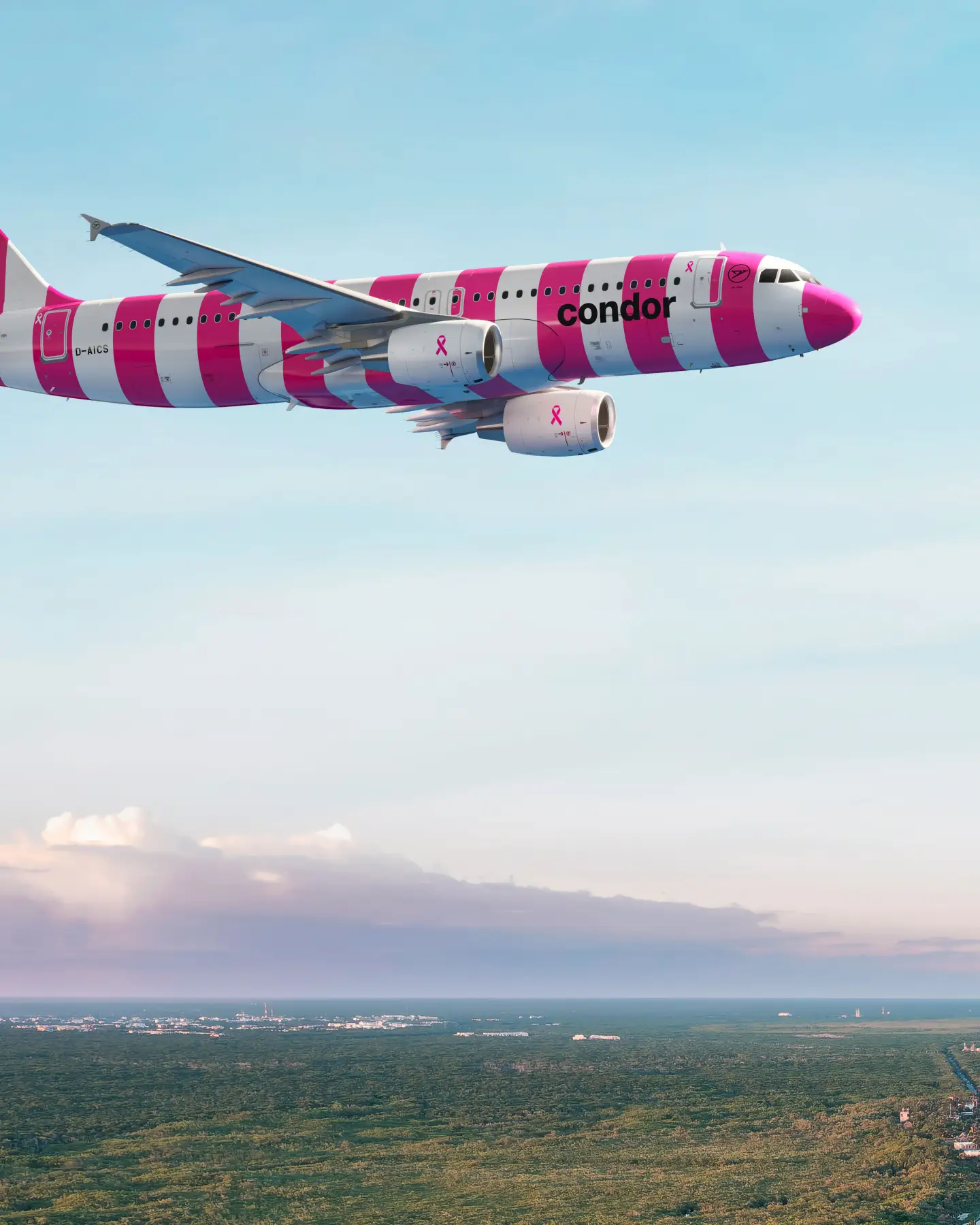 Condor plane with pink and white livery and breast cancer ribbon flies over tropical coast at sunset.