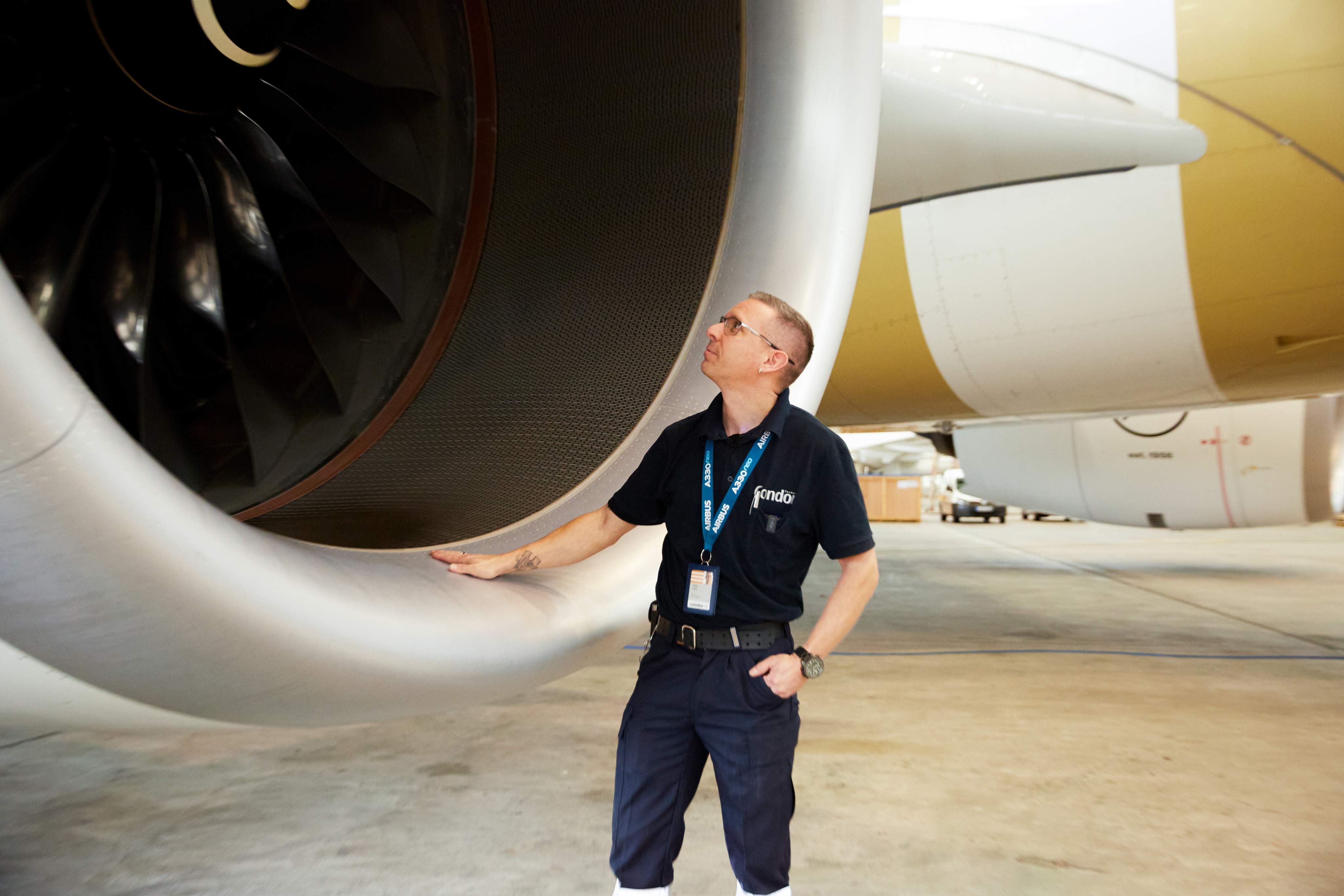 Technik údržby letadel v pracovním oblečení stojí před velkou kulatou leteckou turbínou a dívá se dovnitř.