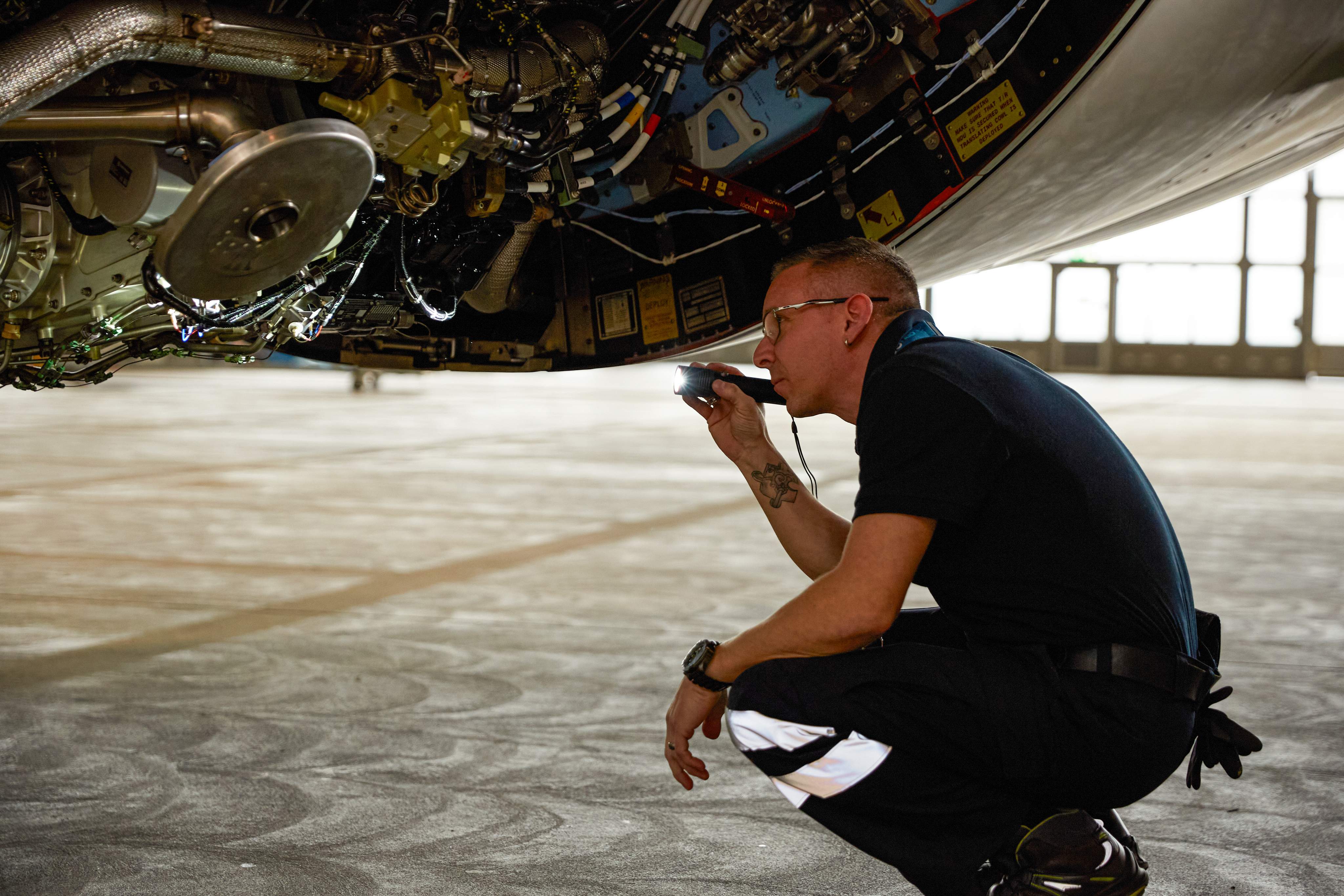 Un technicien aéronautique utilise une torche pour vérifier le train d'atterrissage et les composants du système pendant la maintenance dans le hangar.