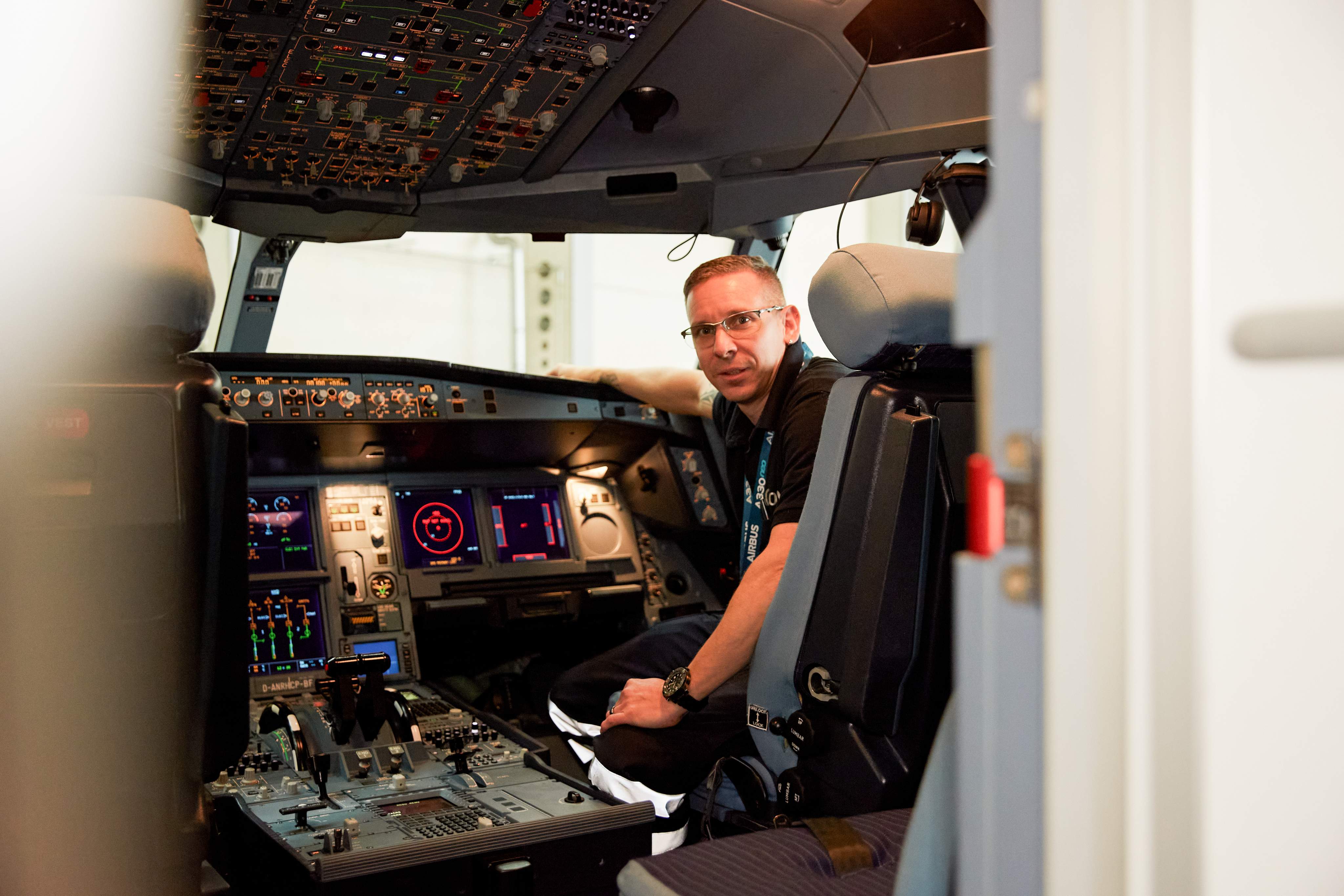 Un mécanicien de systèmes aéronautiques est assis dans le cockpit d’un avion lors d’un test et regarde la caméra.
