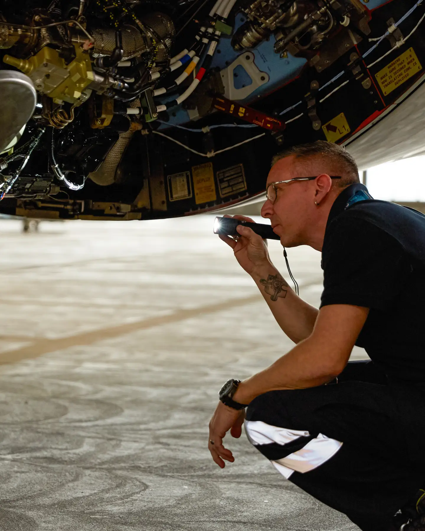 Een vliegtuigtechnicus gebruikt een zaklamp om het landingsgestel en de systeemonderdelen te controleren tijdens onderhoudswerkzaamheden in de hangar.