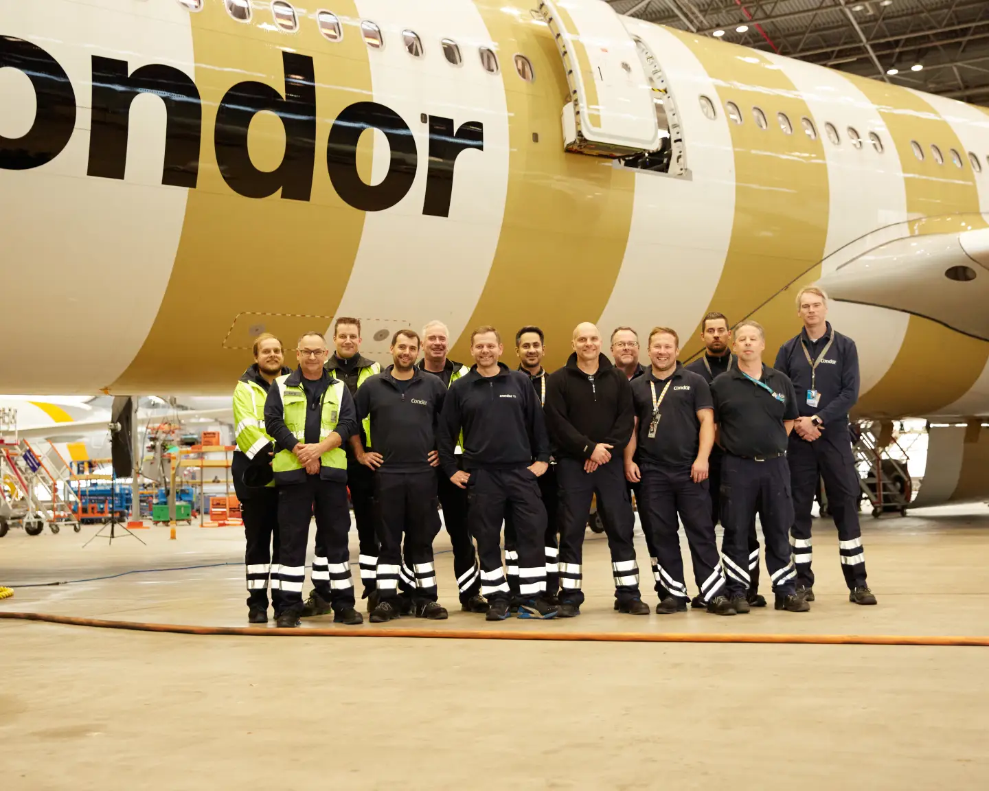 Tým údržby letadel stojí v hangáru před letadlem Condor, na trupu je viditelný nápis „Condor“.