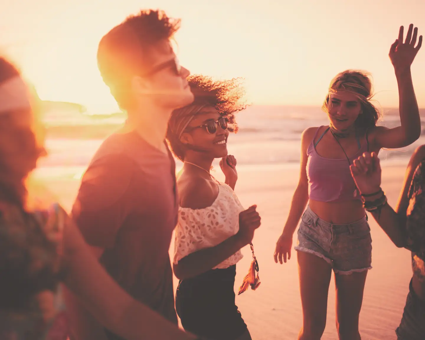 Grupo mixto de personas alegres bailando juntas en una fiesta de playa en una tarde de verano.