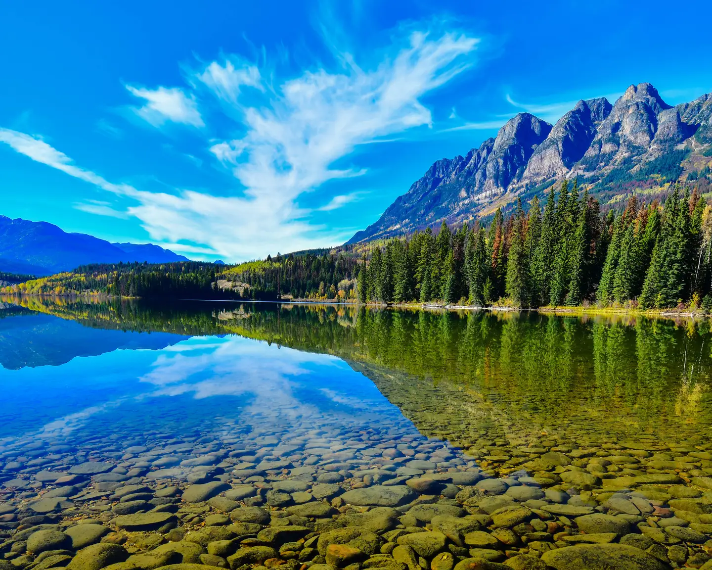 Lago cristalino con montañas y bosques circundantes bajo un cielo azul brillante cerca de Grande Prairie, Canadá.