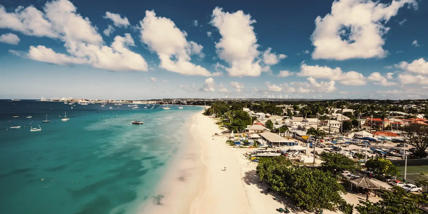 Küstenansicht von Barbados mit verschiedenen Städten entlang des Strandes und einigen Booten auf dem Wasser.
